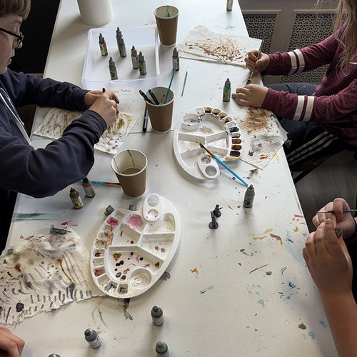 Children painting miniatures with speed paints and brushes on a table.