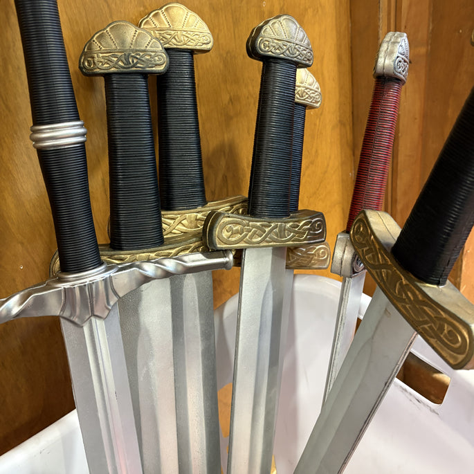 Set of foam swords with ornate handles and sheaths on a wooden stand.
